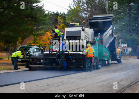 Road construction crew and equipment laying a new asphalt surface on a village street. Stock Photo