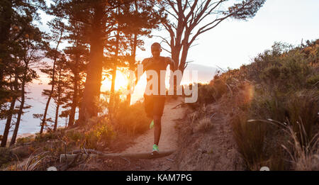 Young man running down a hillside trail at dusk Stock Photo