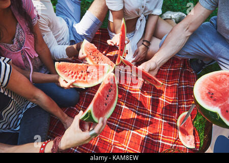 Cheerful friends enjoying watermelon on picnic on sunny summer day Stock Photo