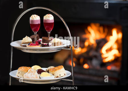 Afternoon tea platter served in front of a roaring orange warm log fire. Stock Photo