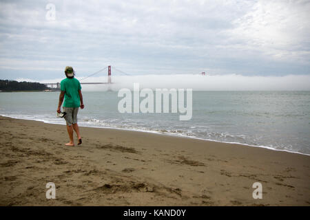 Person walking on beach in front of Golden Gate Bridge, San Francisco, California, USA. Bridge is partially in fog, Stock Photo
