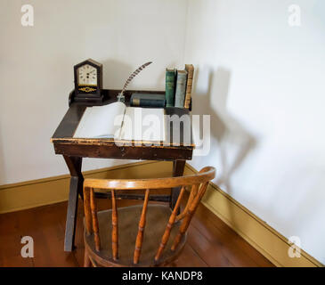 A small vintage desk with a clock, some books, and a quill pen and paper. Stock Photo