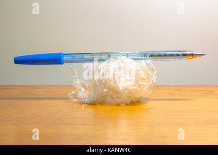 Plastic food wrap crumpled up isolated on background with pen placed on top. Pen and plastic wrap isolated on white background and wood foreground Stock Photo