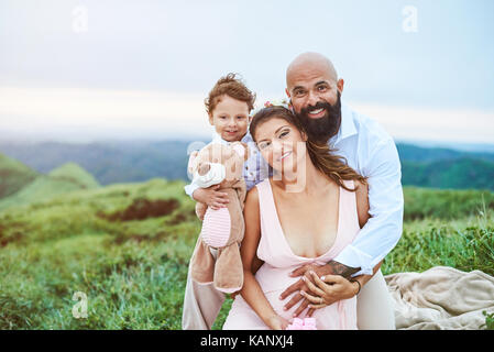 Young happy family sitting on grass in blurred natural background Stock Photo