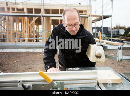 Carpenter Using Table Saw To Cut Plank At Site Stock Photo