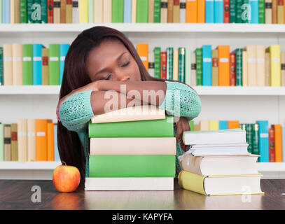 Tired university student sleeping on stacked books at desk in library Stock Photo