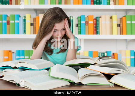 Overburdened schoolgirl looking at books while studying in library Stock Photo