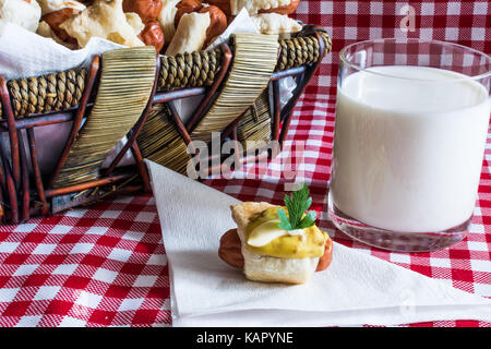 Wicker basket with artisan mini hot dogs (Sausage in the dough) with sausage on a napkin covered in mustard, mayonnaise and a glass of fresh cow's mil Stock Photo