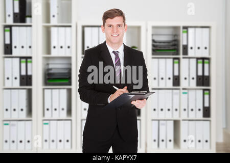 Portrait of young businessman writing on clipboard in office Stock Photo