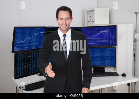 Portrait of confident stock broker offering handshake against multiple monitors in office Stock Photo