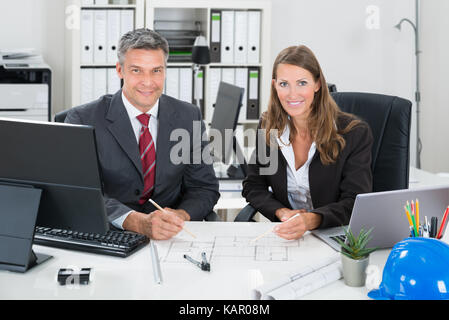 Portrait of male and female architects working on blueprint at desk in office Stock Photo