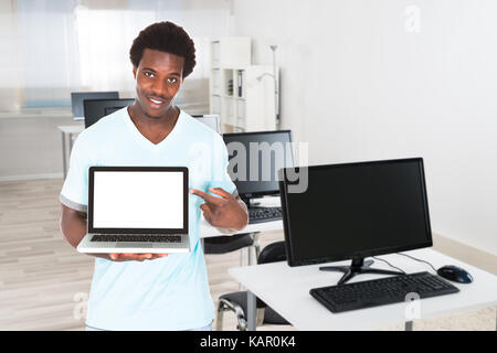 Portrait of confident young male nurse pointing at laptop in clinic Stock Photo