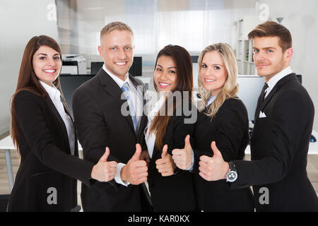 Portrait of happy multiethnic business people gesturing thumbs up in office Stock Photo