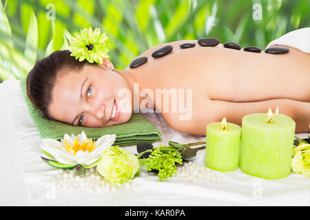 Portrait of happy young woman receiving hot stone therapy in beauty spa Stock Photo