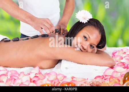 Portrait of smiling young woman getting hot stone therapy at spa salon Stock Photo
