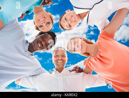 Directly below portrait of happy multiethnic friends forming huddle against sky Stock Photo