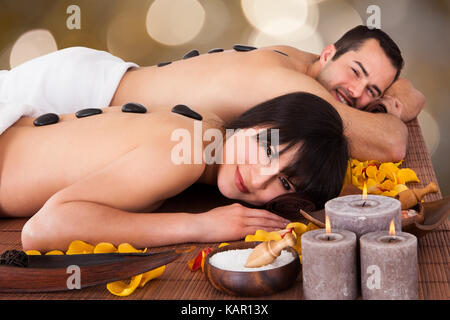 Portrait of happy young couple enjoying hot stone therapy in beauty spa Stock Photo