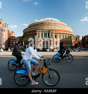 Tourists on rental bike passing by Royal Albert Hall. London's bicycle sharing scheme launched with 6000 bikes on 2010 to help ease traffic congestion Stock Photo