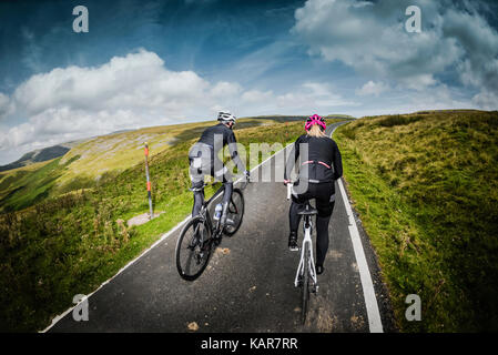 Cycling couple climbing Great Dun Fell in the Pennines, Cumbria, UK Stock Photo
