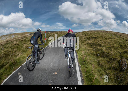 Cycling couple climbing Great Dun Fell in the Pennines, Cumbria, UK Stock Photo