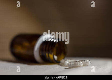 Pills coming out of a little glass bottle on a white surface. Stock Photo