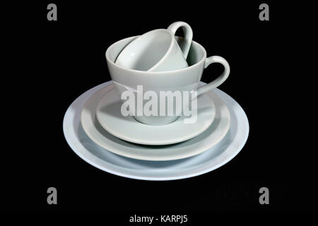 Pile of two white porcelain tea cup with saucers and plate isolated on black background, minimalist image Stock Photo