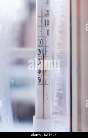 The view through frozen window from room to the outdoor thermometer which showing subzero temperature. Stock Photo