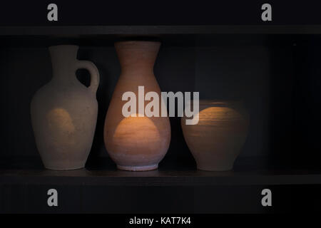 Three terracotta vases earthenware household item handmade on a dark shelf isolated on black. Stock Photo