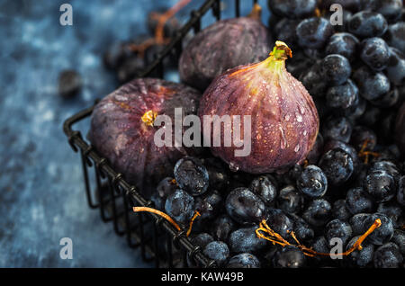 Fresh figs and purple grape in basket on dark wooden background Stock Photo