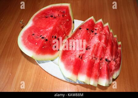 A ripe watermelon is cut and lies on a large white dish. Stock Photo