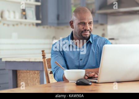 Mature African man using a laptop over breakfast Stock Photo