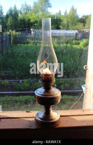 An old-fashioned kerosene lamp stands on a wooden window-sill. Stock Photo
