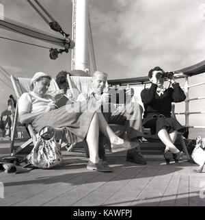 1950s, historical, three passengers on the Union-Castle liner, traveling from Southhampton to Cape Town, relax on the deck, two of them reading and a lady looking through a pair of binoculars. Stock Photo