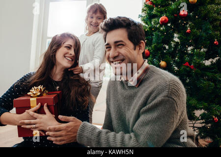 Happy family exchanging gifts sitting beside a Christmas tree . Smiling young woman holding a Christmas gift box. Stock Photo