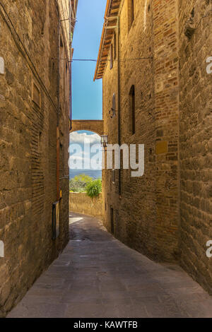 Vertical photo with view into small narrow street. The buildings are build from volcanic tuf stone typical for Tuscany in Italy. The view between hous Stock Photo