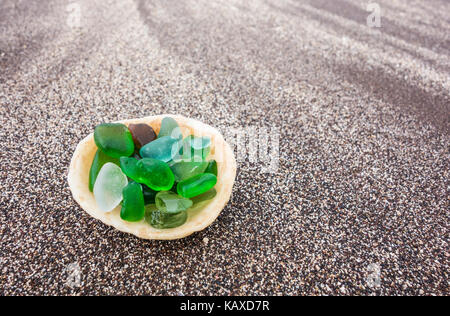 Glass from broken bottles washed on to beach inside shell on beach Stock Photo