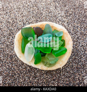 Glass from broken bottles washed on to beach inside shell on beach Stock Photo
