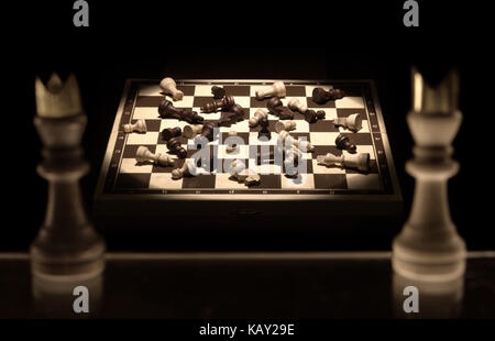 Chess kings on a black background looking over a chessboard battlefield full of victims as a metaphor of the nature of war Stock Photo
