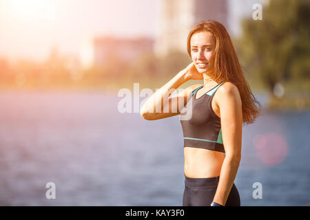 Portrait of young sporty woman resting after jogging in park near lake. Portrait of athletic girl in black top after fitness workout. Healthy lifestyl Stock Photo