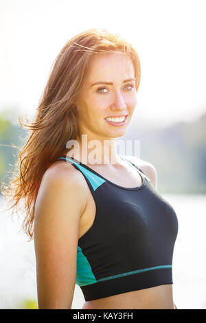 Portrait of young sporty woman resting after jogging in park near lake. Portrait of athletic girl in black top after fitness workout Stock Photo
