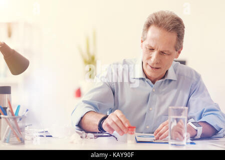 Cheerless sick man taking pills in the office Stock Photo