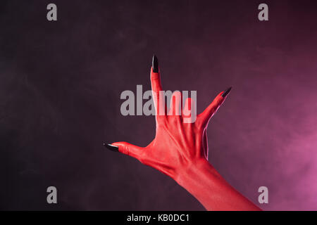 Red devil hand with black nails showing heavy metal symbol, Halloween theme Stock Photo