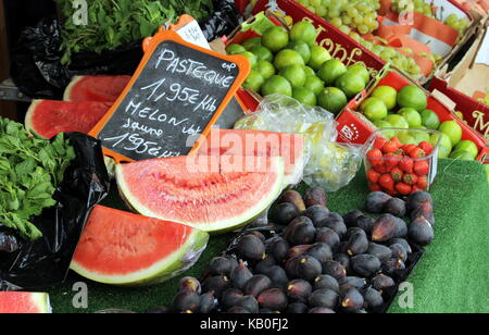 Water melon (French "Pasteque") for sale along with other fruits on a market stall Stock Photo