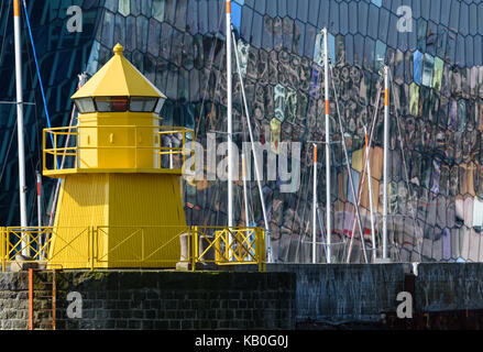 Yellow lighthouse in the Reykjavik, Iceland harbor with colorful and abstract glass exterior of the Harpa concert on the background with reflections i Stock Photo