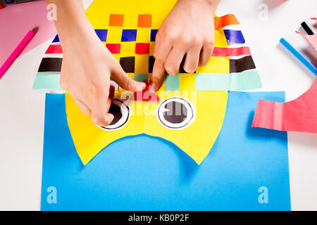 Child making paper crafts. Boy hand's sticking colorful owl made of colored paper Stock Photo