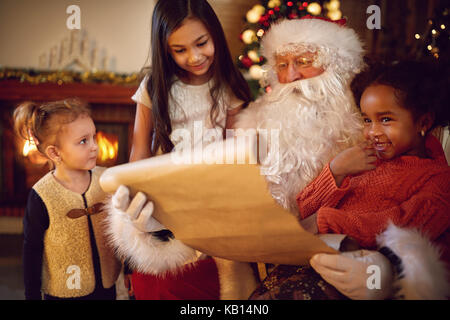 Group of little multi ethnic girls looking in Santa Claus which reading wish list Stock Photo