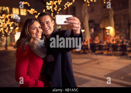 happy moments together. Happy young loving couple making selfie and smiling while standing Christmas background Stock Photo