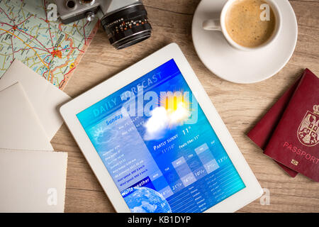 Workplace with tablet pc showing weather forecast and a cup of coffee on a wooden work table Stock Photo