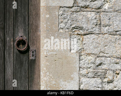 Old weathered wooden door with rusty iron lock and knocker on ancient white stone wall Stock Photo
