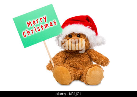 A teddy bear wearing a Santa hat holding a sign with Merry Christmas written on it, isolated on a white background. Stock Photo